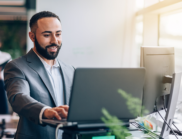 Employee working on two screens, smiling at computer.