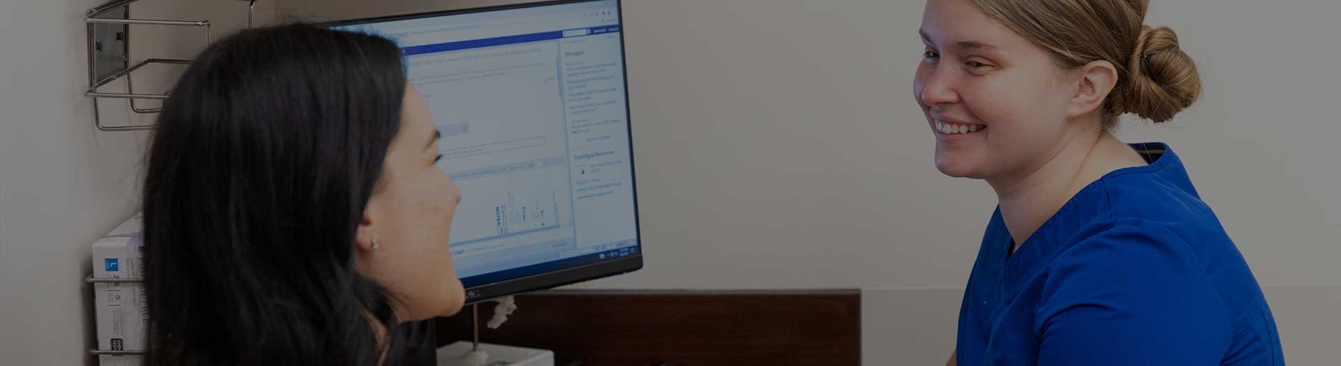 Page Header Image - Ascension Medical Group - Two female medical professionals chatting near computer