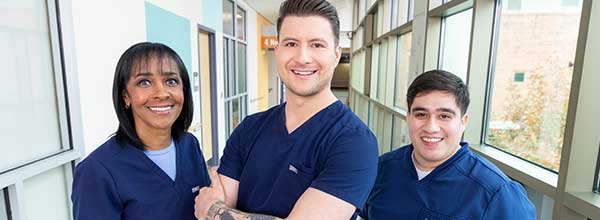 Tile - Ascension Nursing - Diversity and Inclusion - Three medical professionals in hallway smiling into camera