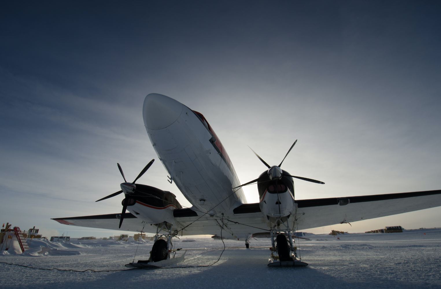 Low-angle view of a twin-propeller aircraft parked on a vast, snow-covered environment