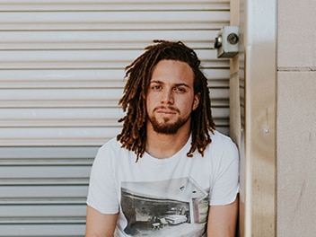 A man in a white t-shirt sitting in front of a metal gate.