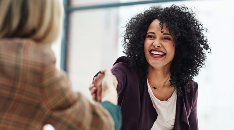 Two colleagues shake hands with happy expressions.