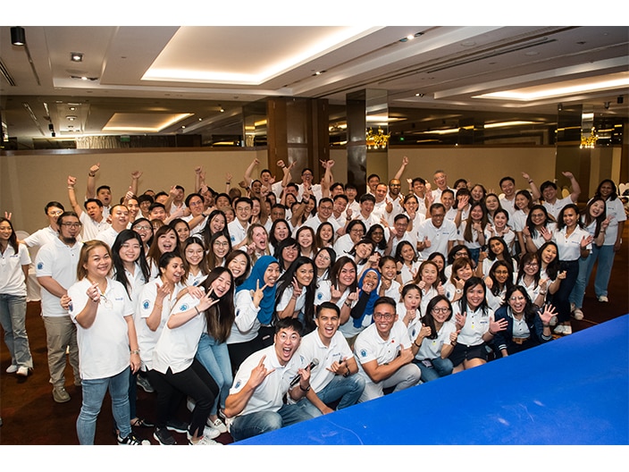 Group of employees celebrating together with a 'win' sign, smiling and posing for the photo.
