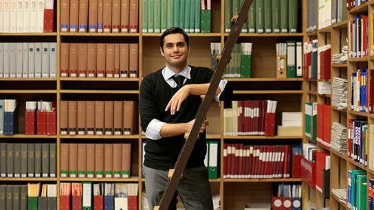 Smiling man standing in front of filing cabinets and leaning against a ladder