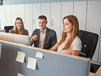 Trois employés souriants sont assis dans le bureau et regardent l'écran.