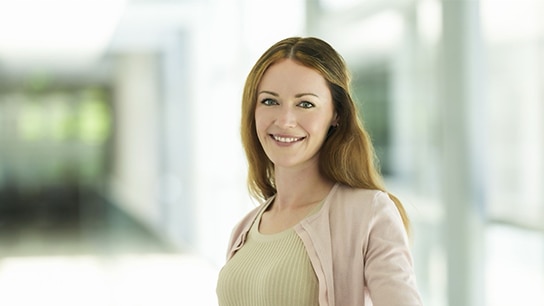 Eine Frau steht lächelend in einem Flur eines Bürogebäudes