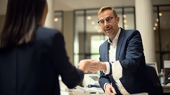 Allianz Mitarbeiter gibt einer anderen Person etwas in die Hand und lächeltt dabei