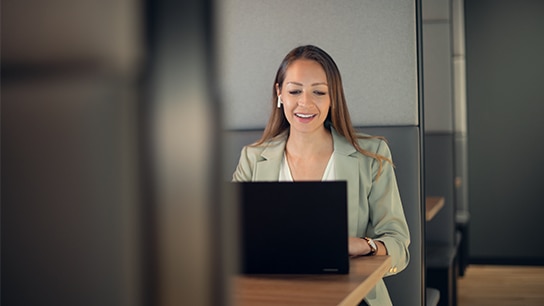Frau sitzt an einem Tisch mit ihrem Laptop und arbeitet