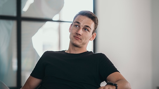 Allianz Mitarbeiter trägt ein schwarzes T-Shirt uns sitzt in einem Bürogebäude