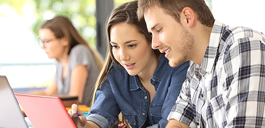 Zwei lächelnde Auszubildende arbeiten zusammen am Laptop