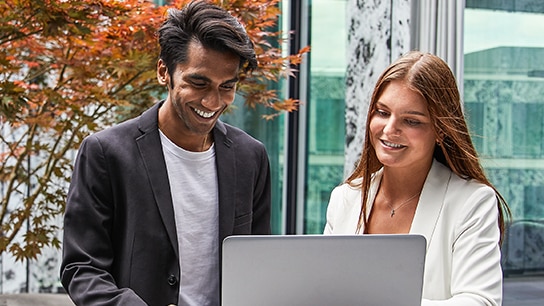 Zwei lächelnde Allianz MItarbeitende arbeiten am Laptop