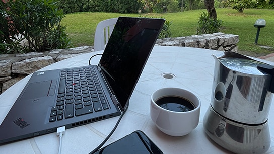 Laptop und Kaffee auf weinem Tisch und im Hintergrund ein Garten 