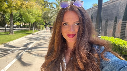 Frau welche mit Sonnenbrille vor einer Promenade mit Bäumen steht
