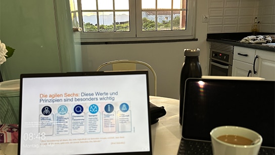 Laptip und ipad auf einem Tisch und im Hintergrund befindet sich die Kü+che sowie eine Ausblick auf eine Landschaft