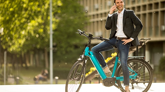 Mann in Jeans und Anzug auf einem blauenm Fahrrad am telefonieren