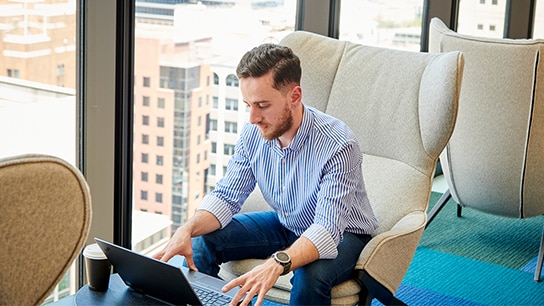 Collaborateur d'Allianz assis sur un fauteuil pendant qu'il travaille sur son ordinateur portable