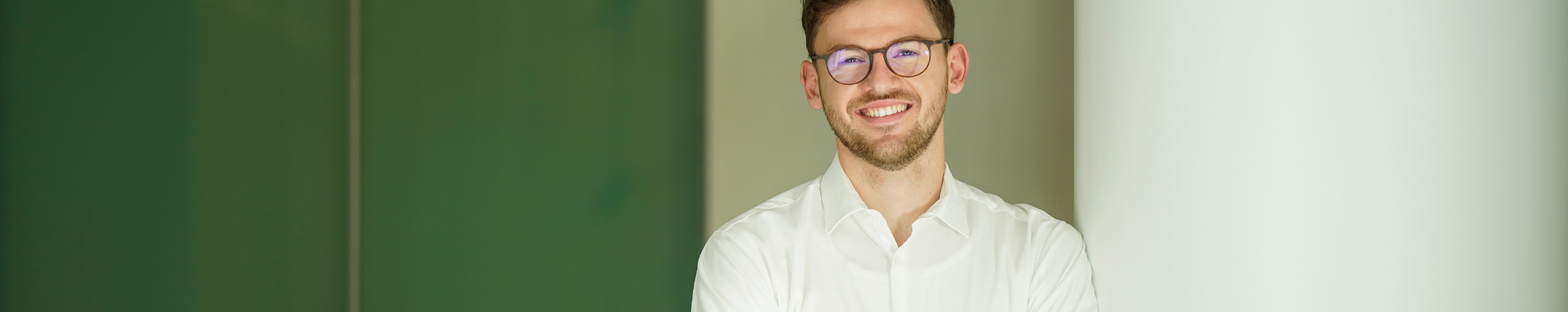 Mann mit Hemd und Brille vor einem Büroraum am lächeln