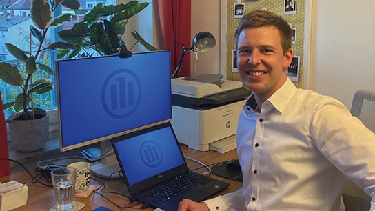 Mann sitzt im Homeoffice mit zwei Bildschirmen und lächelt