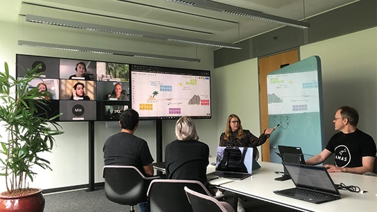 Mitarbeiter arbeiten gemeinsam auf hybridem Weg im Büro und Online zusammen bei einer Besprechung über Teams 