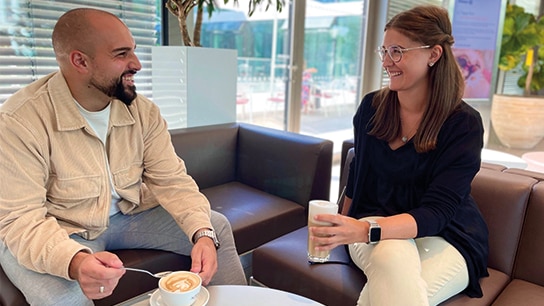 Zwei Allianz Kollegen sitzen auf dem Sofa und trinken Kaffee