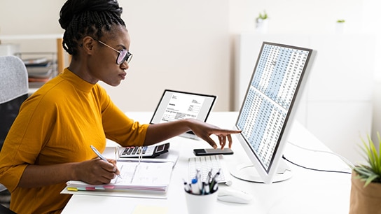 A student analsying a chart in the laptop and taking down notes in a physical notebook