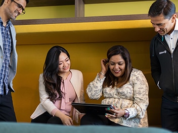 A team of colleagues sharing a joyful conversation while gathered around a laptop, engaged and smiling as they interact.