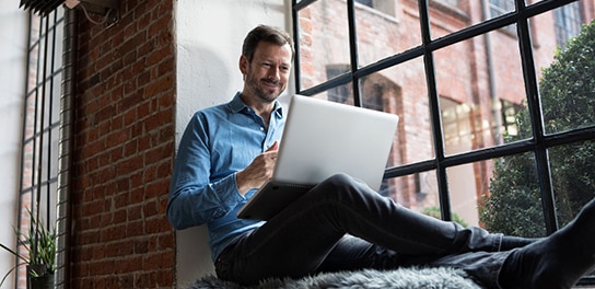 A businessman attending a webinar on his laptop while sitting by the window, engaged in the session