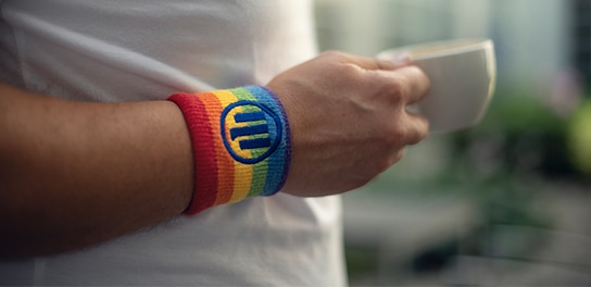 A person's hand holding a cup of tea, wearing a rainbow-colored wristband featuring the Allianz logo.