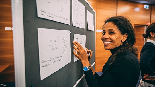 Um colega mais velho sorri para a câmera enquanto publica um aviso no quadro.