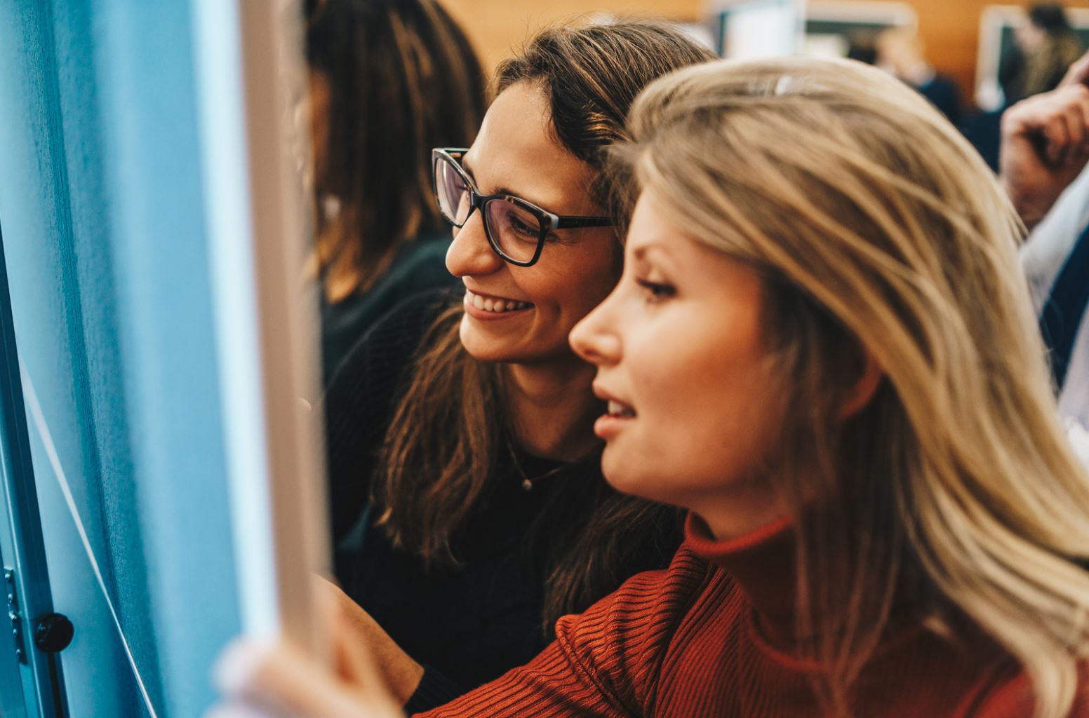 Dois colegas olhando para o quadro de avisos e sorrindo.