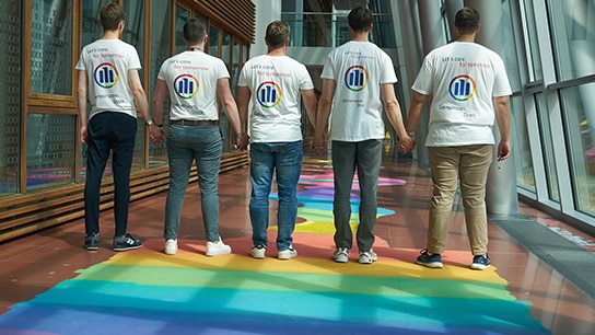 Team steht auf einem Pride Flur und trägt Tshirts mit einem Allianz Pride Logo