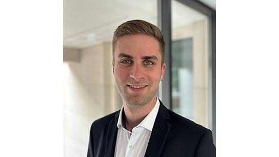Mann lächelt und trägt einen Anzug vor einem Büroraum