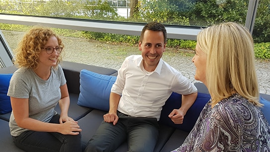 Mehrere Personen besprechen etwas auf einem Sofa in einem Büroraum