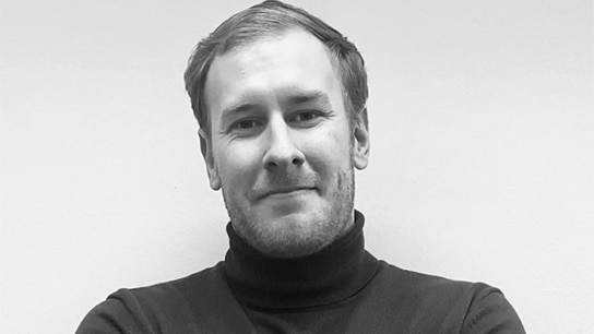 Mann mit Rollkragenpullover vor einer schwarzen Wand