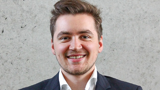 Mann steht mit Anzug vor einer grauen Wand