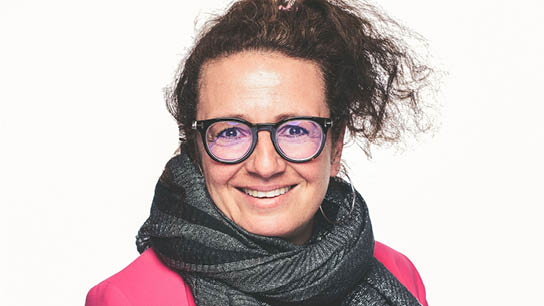 Frau mit Dutt, rosa Pullover und Schal vor einer weißen Wand