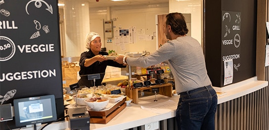 Un employé de la cantine tend un plateau de nourriture à un autre employé.