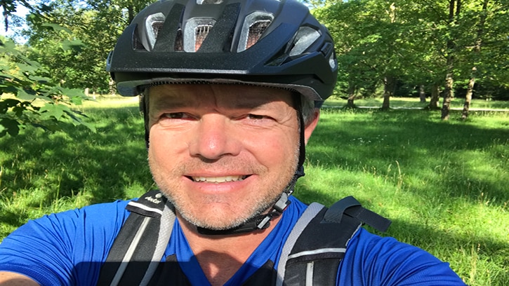 Mann mit Fahrradhelm vor einer grünen Wiese in der Natur