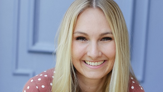 Blonde Frau lächelt vor einer blauen Türe