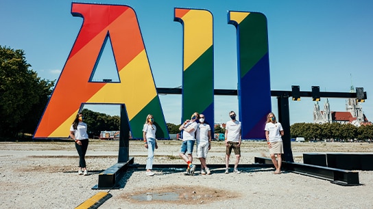 Menschen vor einem großen Allianz Schriftzug in Pride Farben
