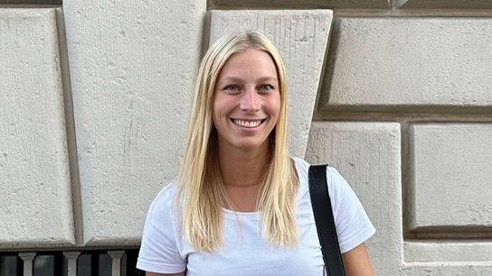 Frau steht vor Gebäude und lächelt