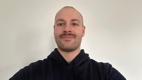 Mann in schwarzem Pullover steht vor weißer Wand