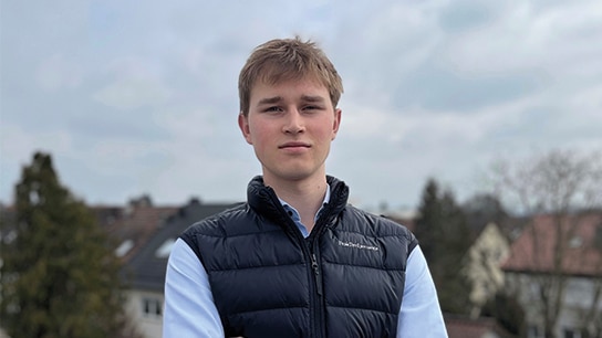 Mann steht draußen und im Hintergrund sind Häuser