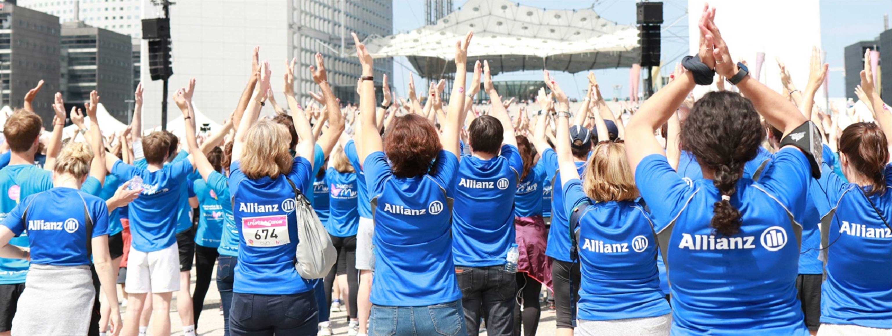 De nombreux employés d'Allianz en T-shirts bleus Allianz, les mains en l'air lors d'un événement.
