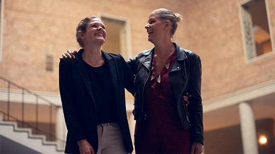 Katharina and her colleague smiling happily, with a hand on each other's shoulder.