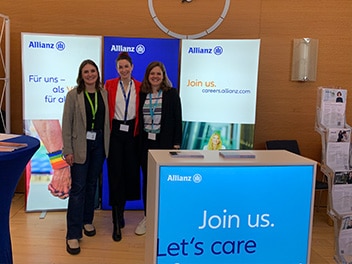 Drei lächelnde Mitarbeitende an einem Allianz Messestand