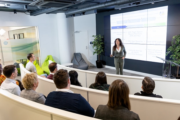 A woman standing in front of several people on the podium and presenting