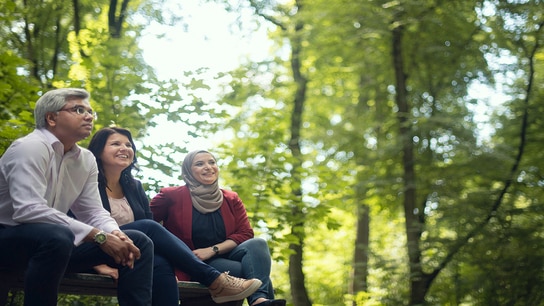 Three people sitting together on a bench surrounded by nature