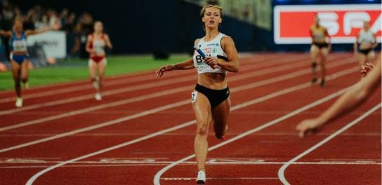 A female athlete running on a track, surrounded by fellow competitors in an energetic race atmosphere
