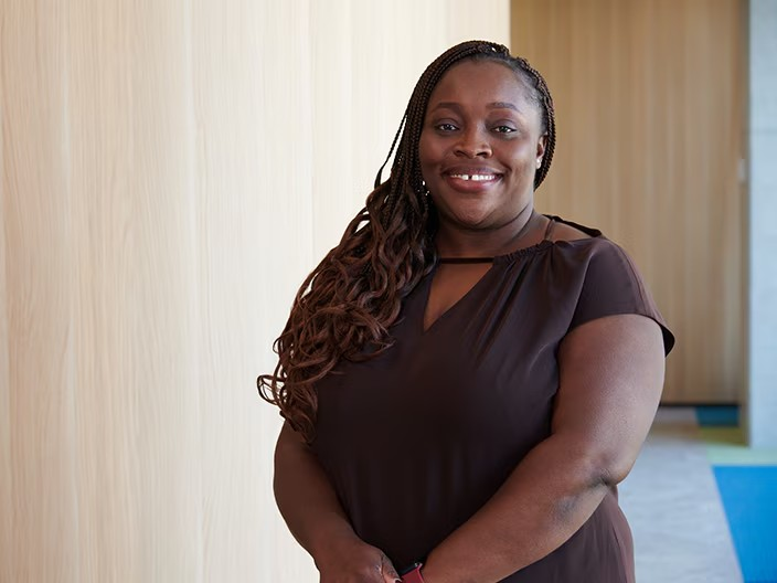 A woman in a brown shirt is positioned in an office setting, exuding professionalism and focus